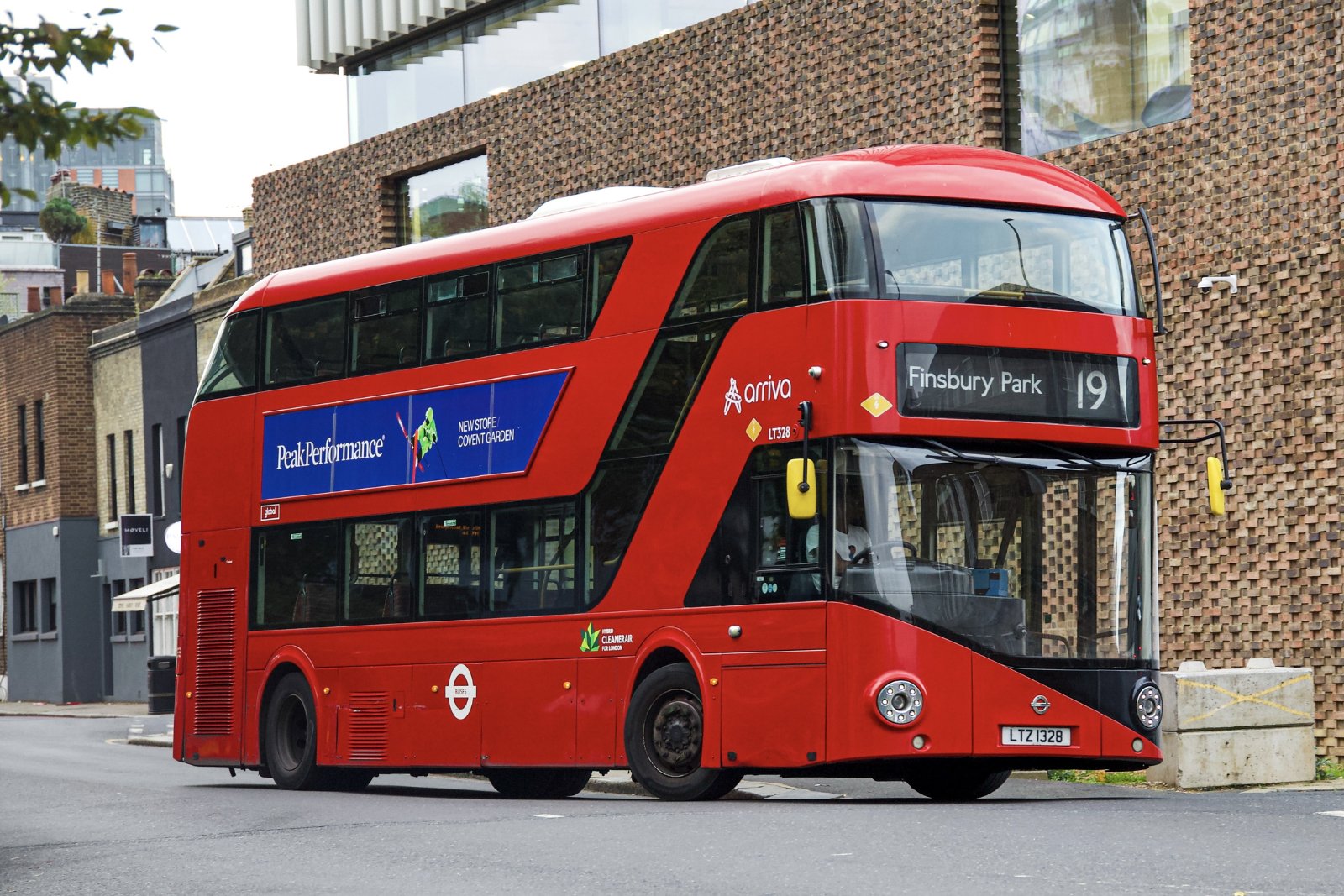 A red London double-decker bus on route 19 to Finsbury Park, driving past a brick building