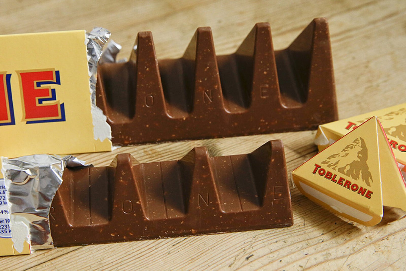 Two opened Toblerone bars showing their row of triangular chocolate peaks, beside a small Toblerone pack on a wooden table