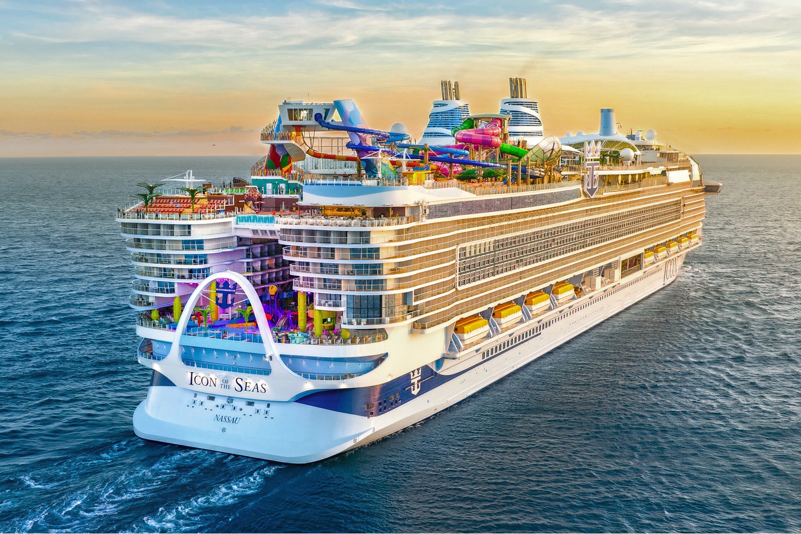 The cruise ship Icon of the Seas at sea at sunset, seen from behind, with bright water slides and pools on its top decks